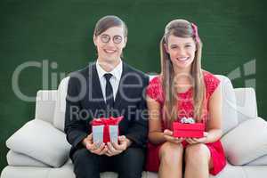 Composite image of cute geeky couple smiling and holding gift