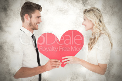 Composite image of attractive young couple holding red heart