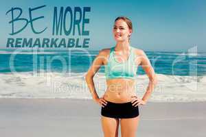 Composite image of fit woman standing on the beach with hands on