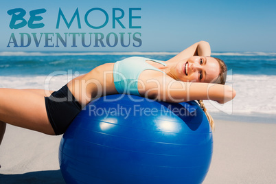 Composite image of fit woman lying on exercise ball at the beach
