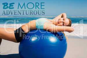 Composite image of fit woman lying on exercise ball at the beach