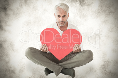 Composite image of upset man sitting holding heart shape Composite image of upset man sitting holding heart shape