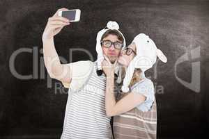 Composite image of geeky hipster couple taking selfie with smart