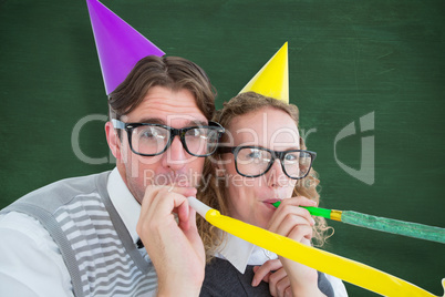 Composite image of geeky hipster couple blowing party horn