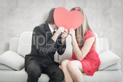 Composite image of cute geeky couple kissing and holding heart o