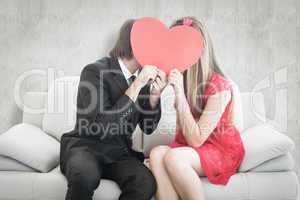 Composite image of cute geeky couple kissing and holding heart o