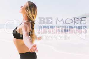 Composite image of fit blonde standing on the beach with arms ou