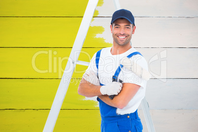 Composite image of smiling handyman with paint roller standing b