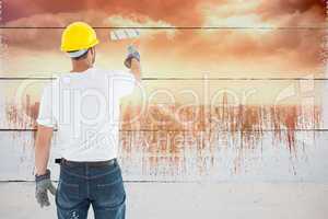 Composite image of man wearing hardhat while using paint roller