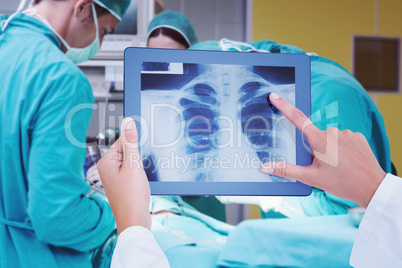 Composite image of doctor looking at xray on tablet