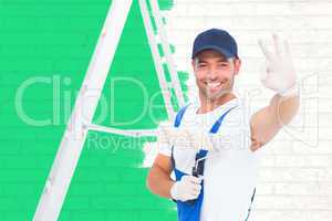 Composite image of happy handyman with paint roller gesturing ok