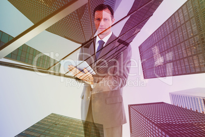 Composite image of serious charismatic businessman holding a tab