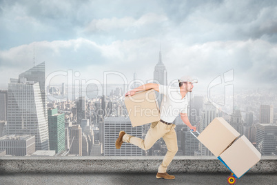 Composite image of delivery man with trolley of boxes running