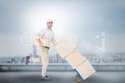 Composite image of happy delivery man with trolley of boxes runn