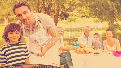 Father and son at barbecue grill with family having lunch in par