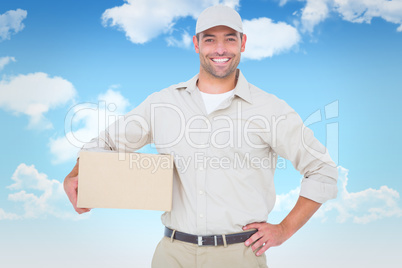 Composite image of confident delivery man with cardboard box on