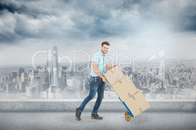 Composite image of happy delivery man pushing trolley of boxes