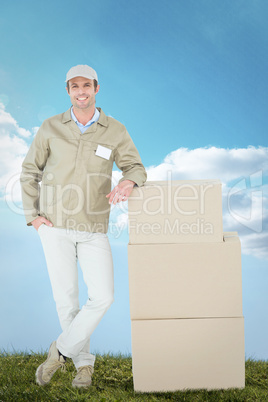 Composite image of confident delivery man standing by stack of b