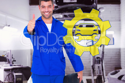 Composite image of mechanic with tire gesturing thumbs up