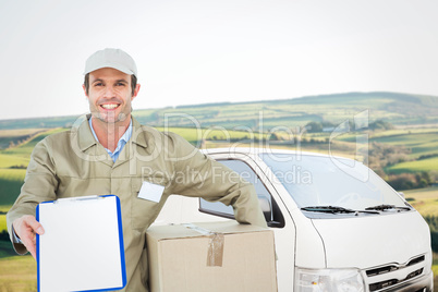 Composite image of happy delivery man with box showing clipboard