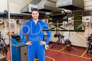 Composite image of smiling mechanic with hands on hips standing