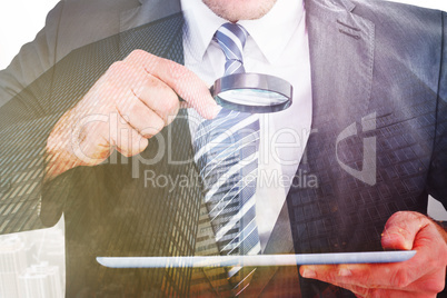 Composite image of businessman looking at tablet with magnifying