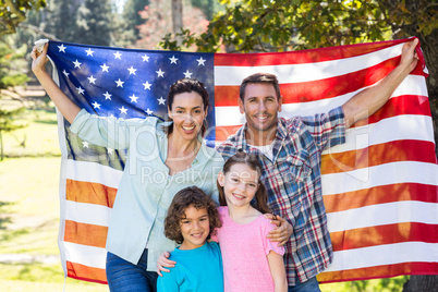 Happy family smiling with an american flag in a park