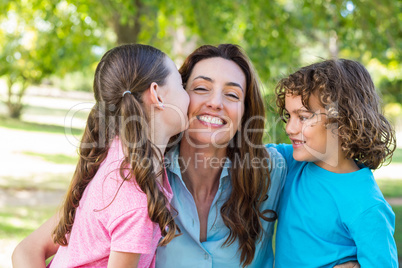 mother and children smiling and kissing in a park