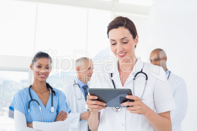 Confident female doctor holding tablet with her team behind