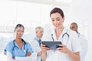 Confident female doctor holding tablet with her team behind