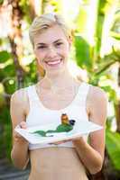 Happy blonde woman presenting plate with herbal medicine