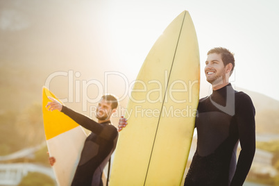 Two men in wetsuits with a surfboard on a sunny day