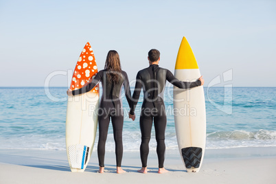 happy couple in wetsuits with surfboard on a sunny day