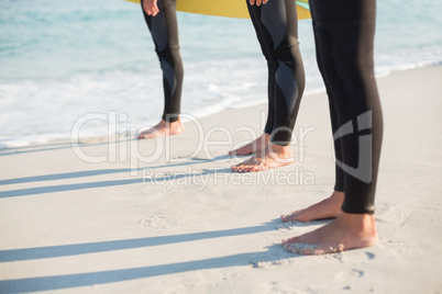 Group of friends on wetsuits with a surfboard on a sunny day