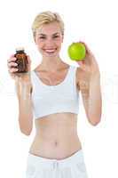 Fit blonde woman holding medicine and green apple