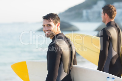 Two men in wetsuits with a surfboard on a sunny day