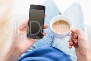 Woman using her mobile phone and holding cup of coffee