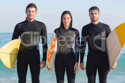 Group of friends in wetsuits with a surfboard on a sunny day