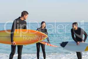 Group of friends on wetsuits with a surfboard on a sunny day