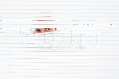 Curious blonde woman looking through venetian blind