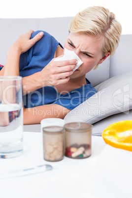 Sick blonde woman blowing her nose and looking at pills