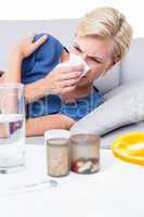 Sick blonde woman blowing her nose and looking at pills