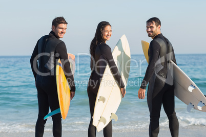 Group of friends on wetsuits with a surfboard on a sunny day