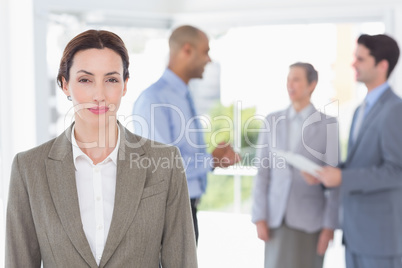 Businesswoman smiling at camera while her colleagues discussing