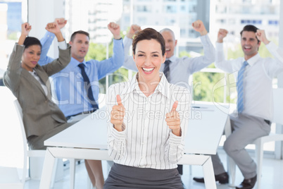 Smiling businesswoman giving thumbs up with her team behind