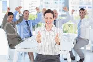 Smiling businesswoman giving thumbs up with her team behind