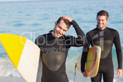 Two men in wetsuits with a surfboard on a sunny day