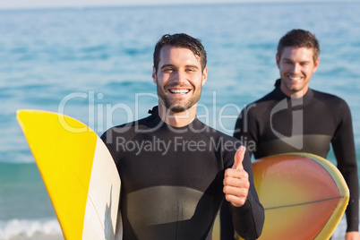 Two men in wetsuits with a surfboard on a sunny day