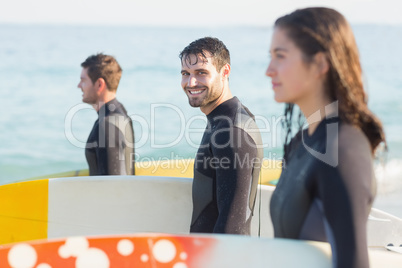 Group of friends on wetsuits with a surfboard on a sunny day