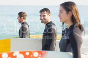 Group of friends on wetsuits with a surfboard on a sunny day